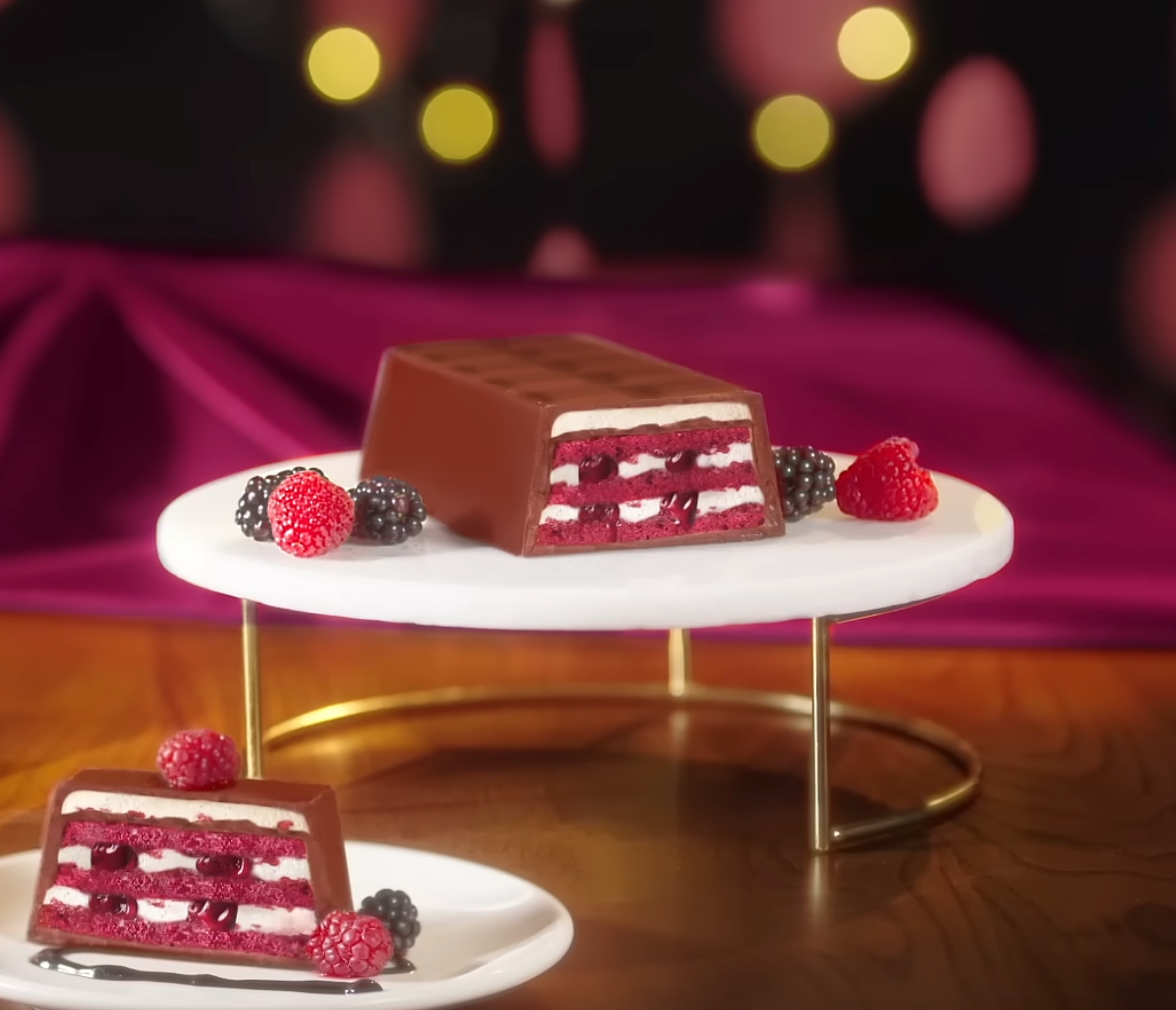 Chocolate cake with red berries on a white stand against a blurred background. Ulker Milk Chocolate Cake with Velvety Red Velvet Base and Forest Berry Sauce – 13.9 oz (395 G)