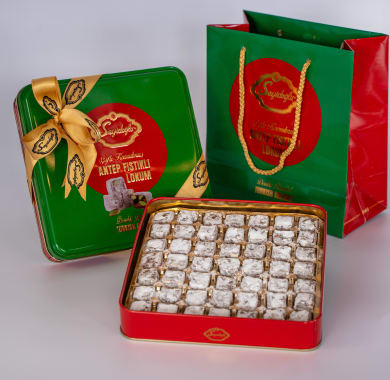 Assorted candies in a red tin with a green decorative box and red bag on a white background